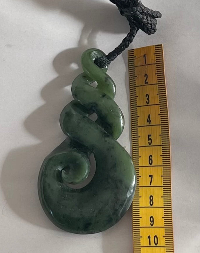 A twist Greenstone Pounamu necklace displayed next to a measuring tape, showing its approximate size.
