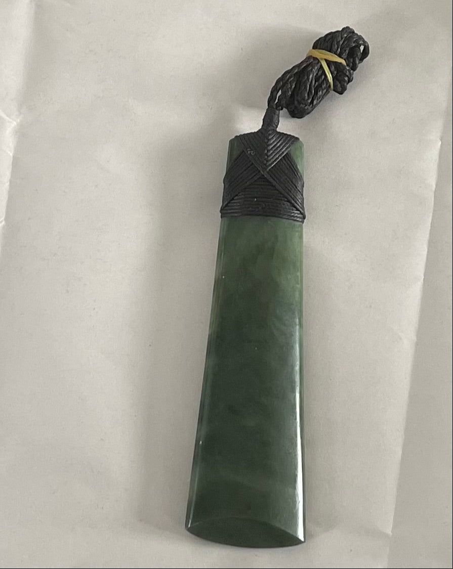 Greenstone Toki pendant with black cord on a white background