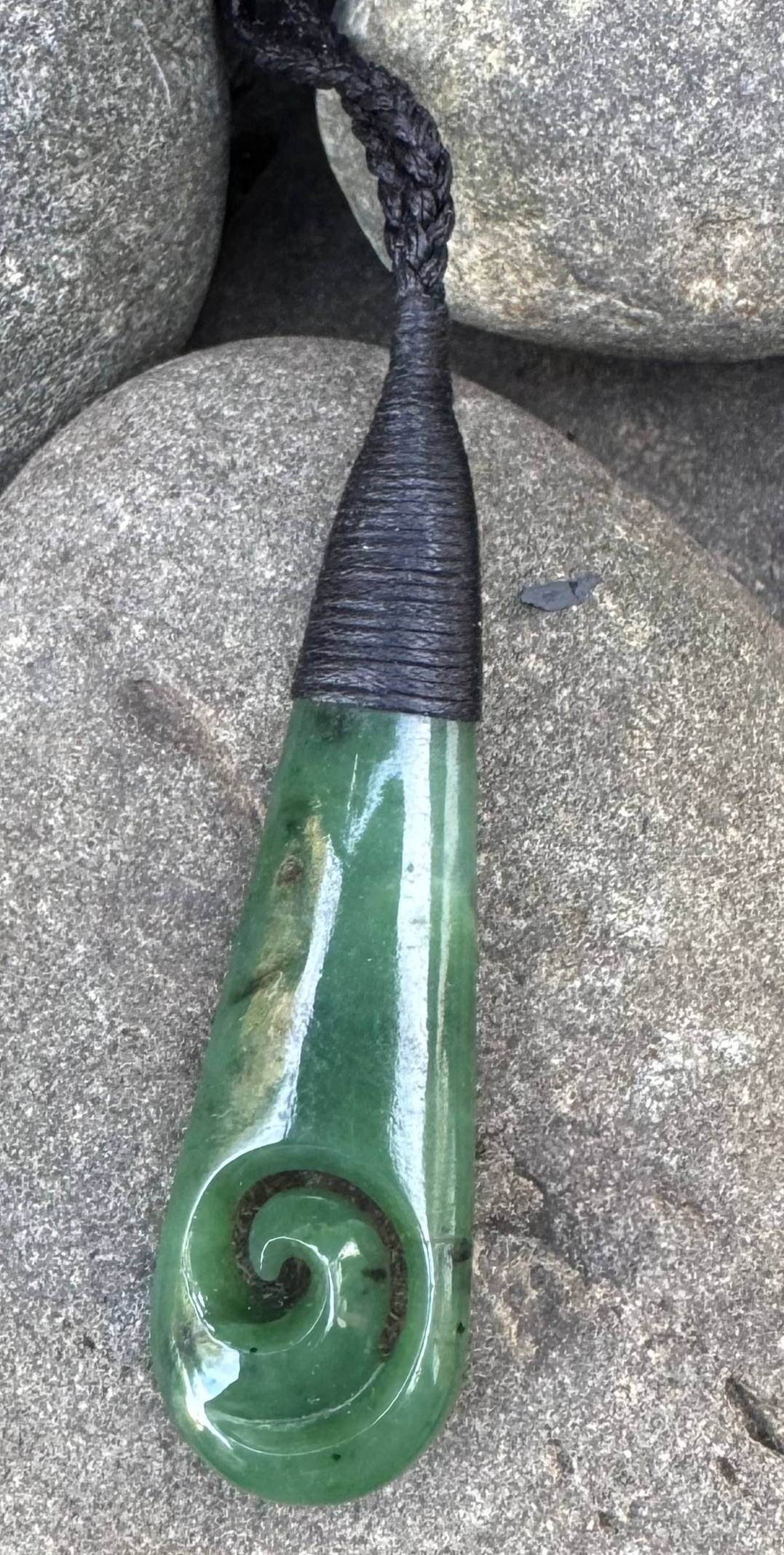 Greenstone necklace carving with black cord on a stone surface