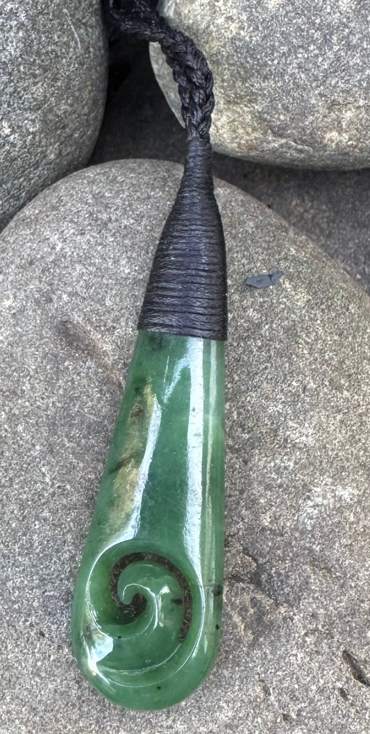 Greenstone necklace carving with black cord on a stone surface