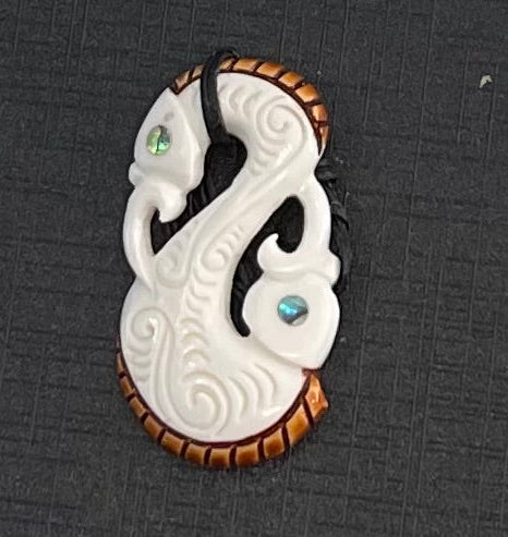 A bone-shaped necklace with a white and brown color scheme, featuring a manaia design and a small teardrop-shaped pendant.