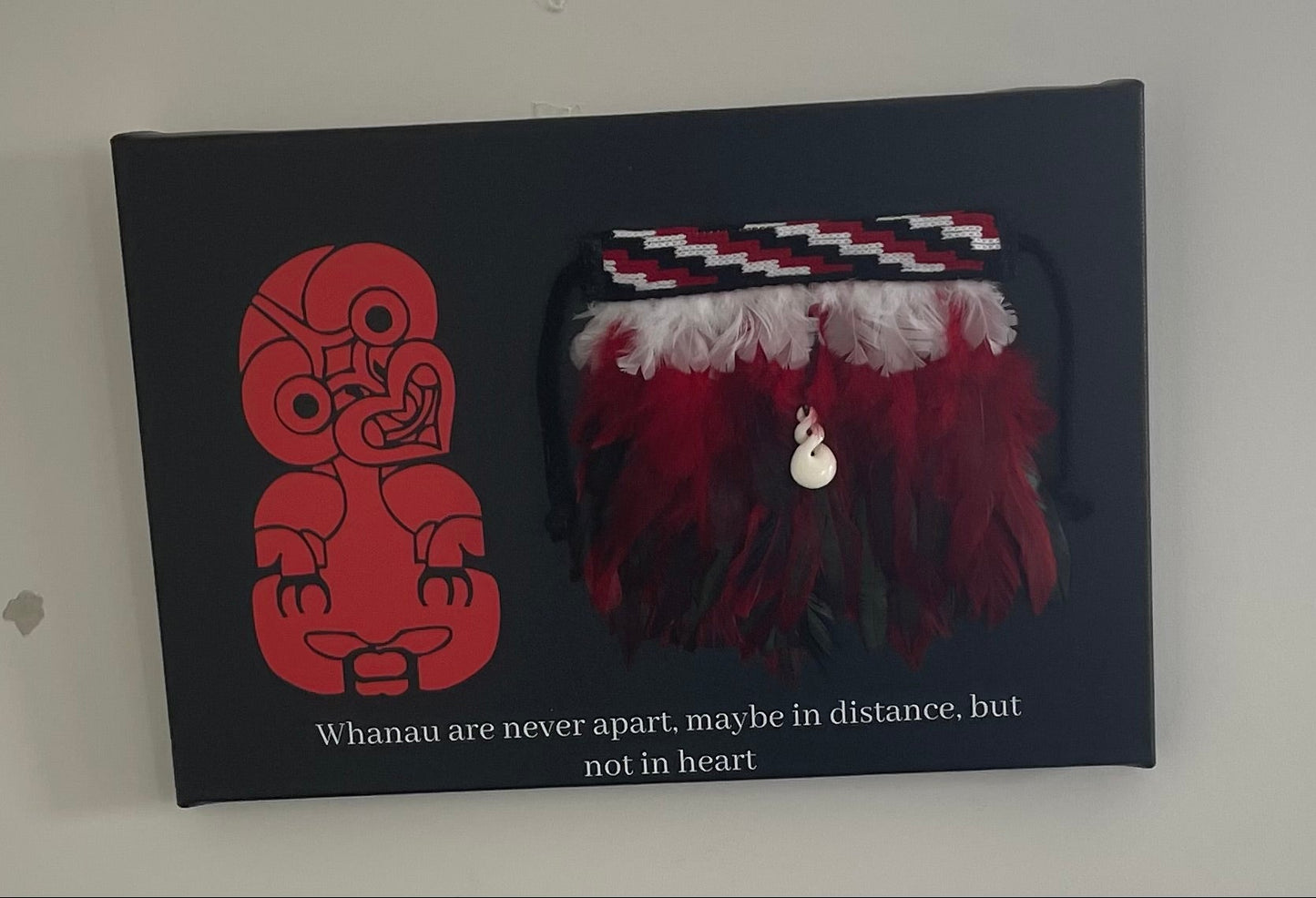 A piece of artwork featuring a korowai design on canvas with a red and black color scheme, including a saying in white text.
