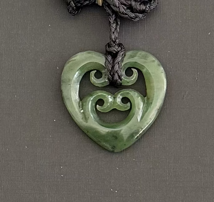 Green jade heart-shaped pendant with intricate designs on a gray background