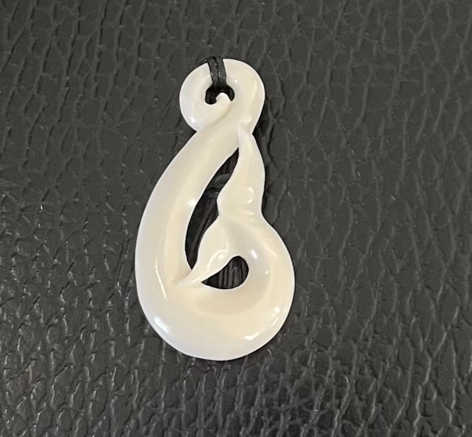 White whale tail bone pendant on a textured black surface