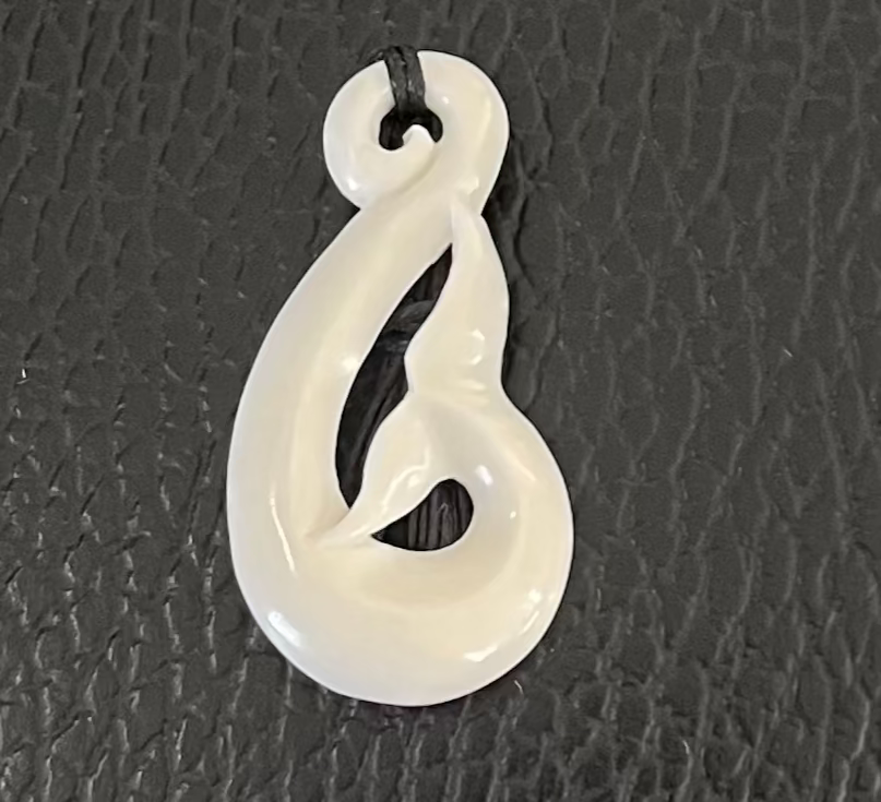 White whale tail bone pendant on a textured black surface