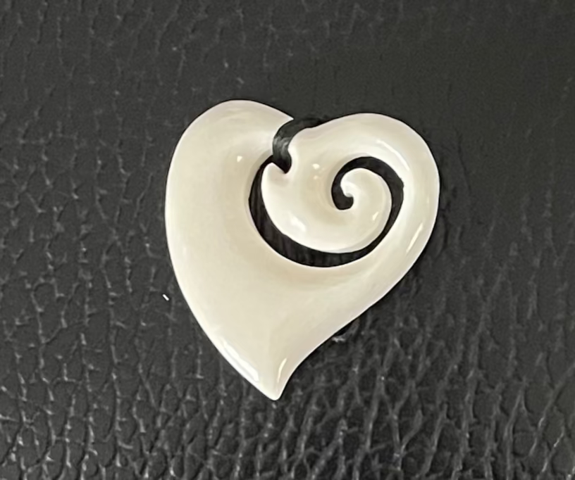 Heart-shaped bone pendant with a spiral design on a black textured background