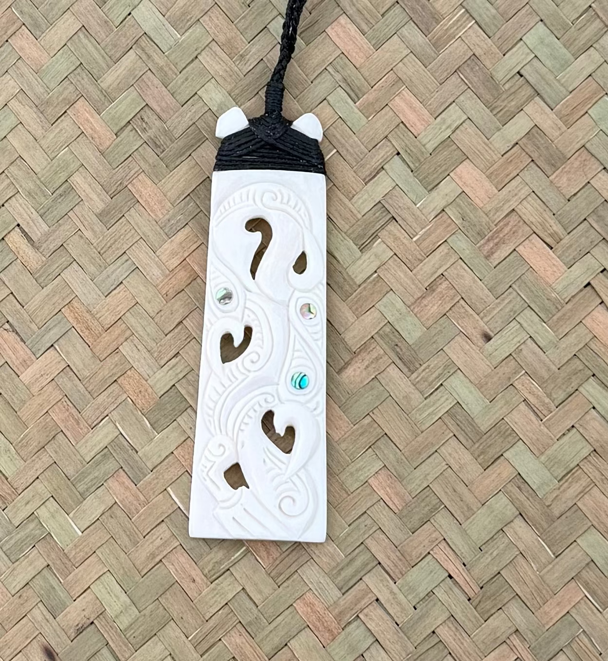 White bone carved pendant with cut-out designs and beads on a black cord against a woven background