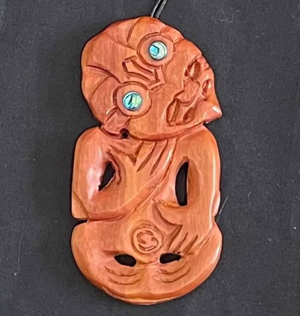 Wooden pendant with intricate carvings and paua on a black background
