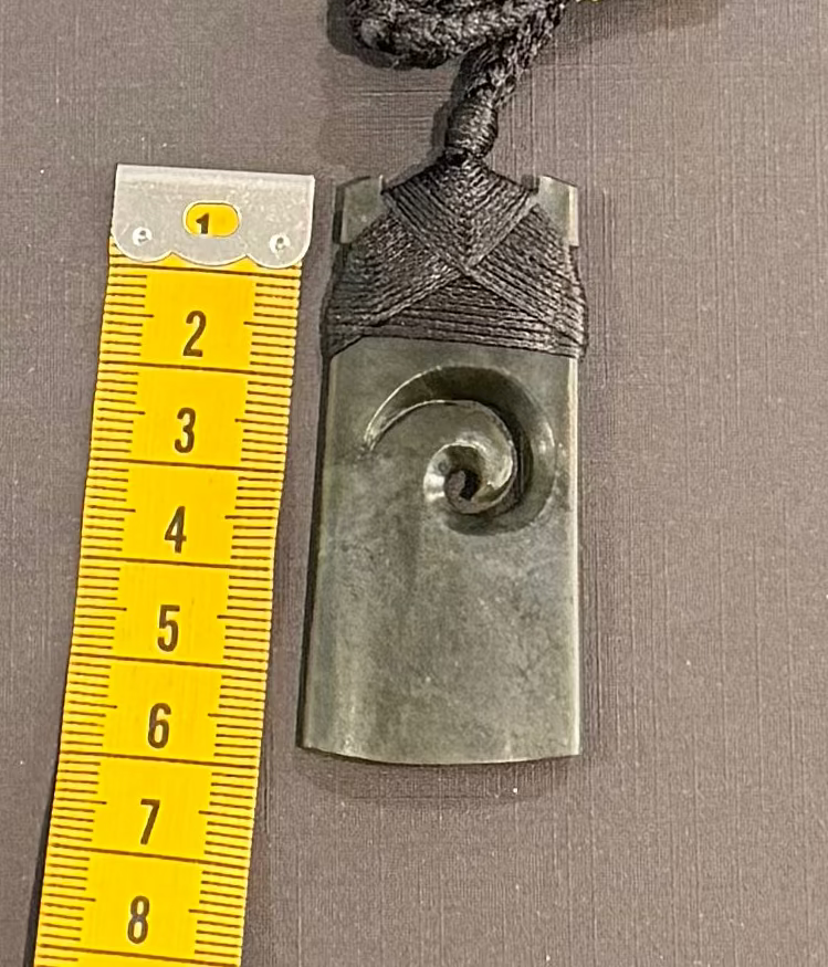Necklace with a spiral pendant next to a yellow measuring tape on a gray background