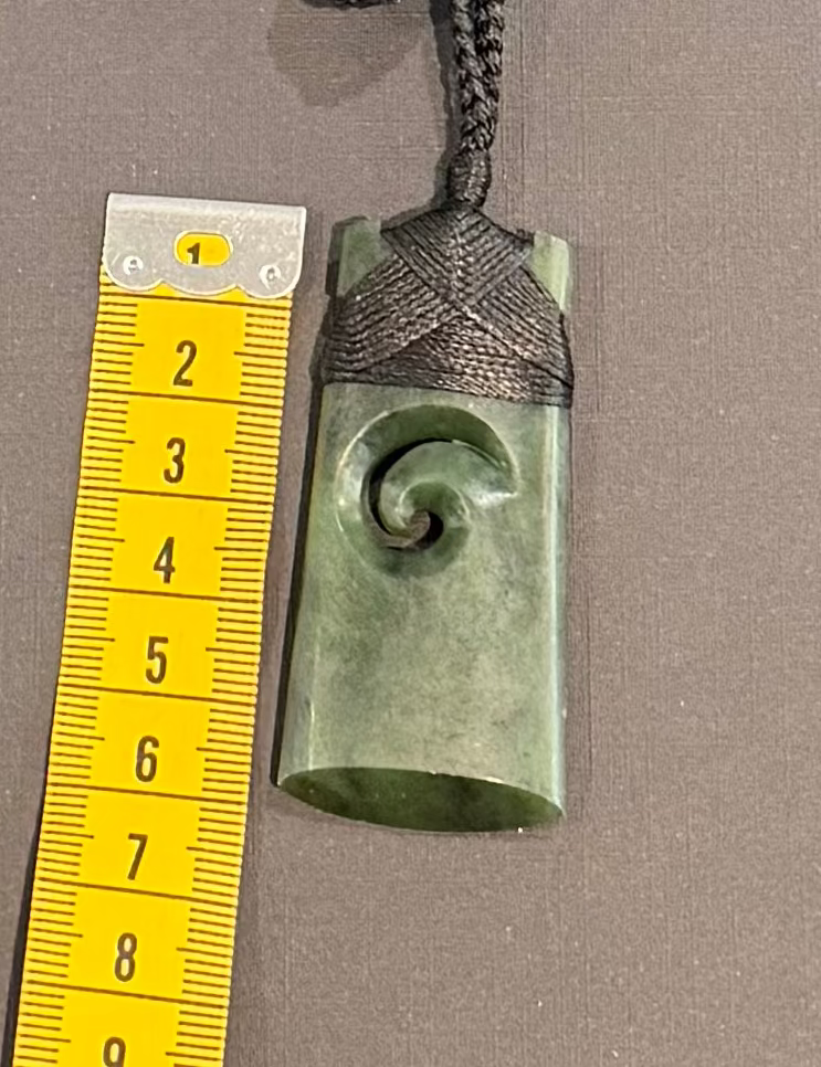 Green jade pendant with spiral design on a string, next to a yellow measuring tape for scale.