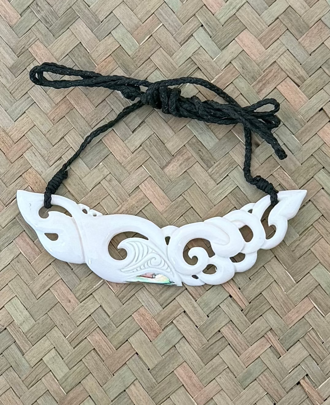 White bone breastplate pendant item with black string on a woven mat