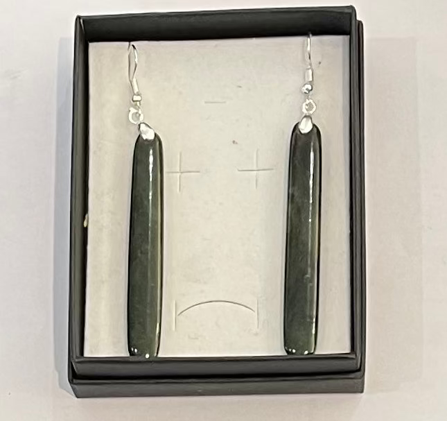 Pair of long, dark greenstone earrings in a black box on a white background