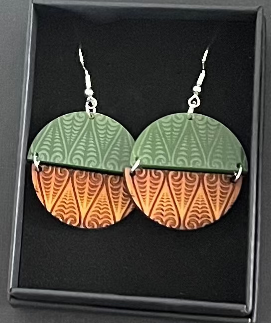 Pair of earrings with green and orange design in a black box on a gray background