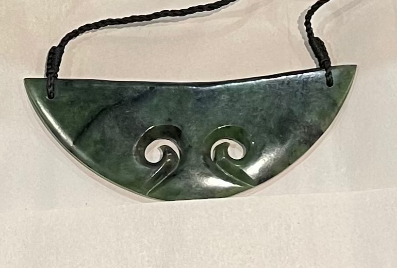 Greenstone breastplate necklace with spiral design on a white background
