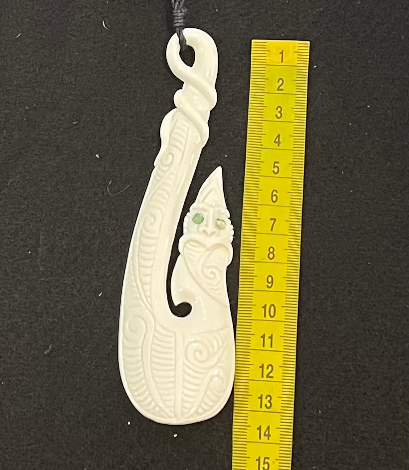 Carved bone hook pendant next to a yellow ruler on a black background
