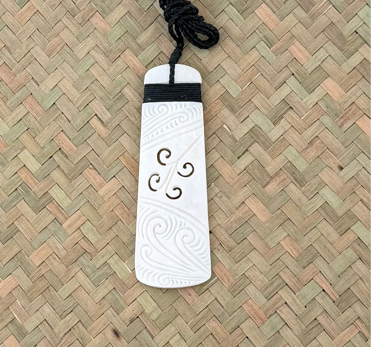 White TOKI KORU BONE pendant with intricate designs on a black cord against a woven background