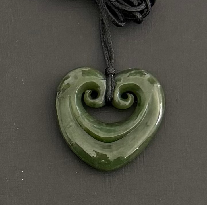 Greenstone jade heart-shaped pendant with spiral design on a dark background