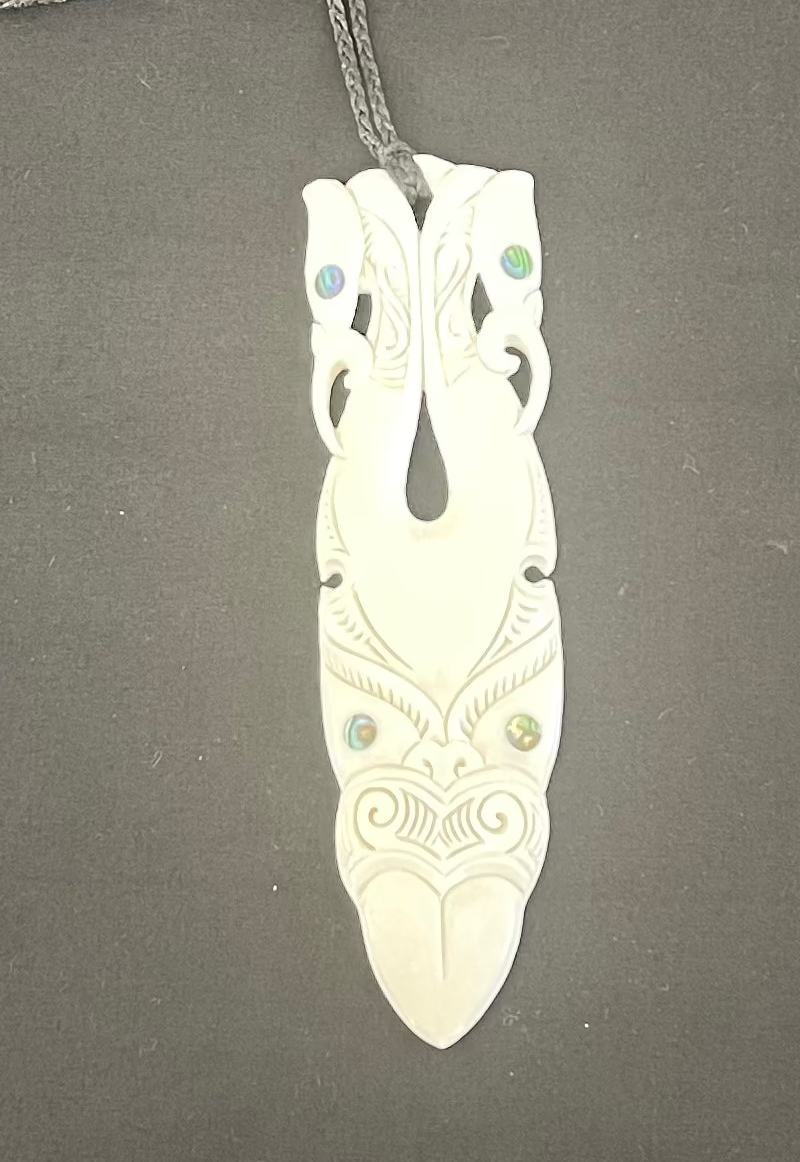 Carved bone pendant with intricate designs on a gray background