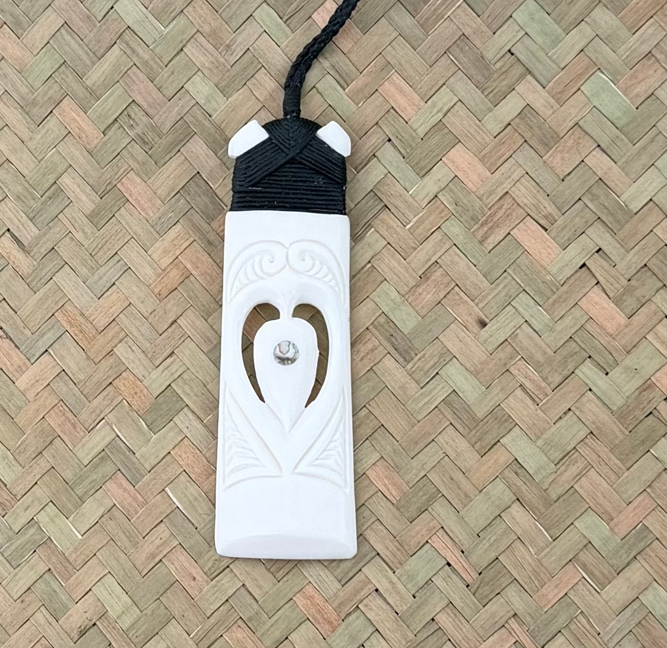 White bone toki pendant with black cord on a woven mat background