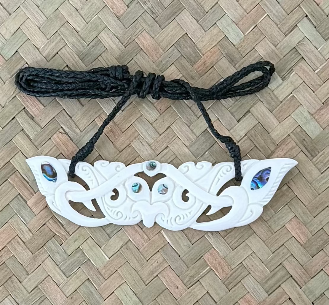 DecorativeMANAIA BREASTPLATE with black cord on a woven mat background
