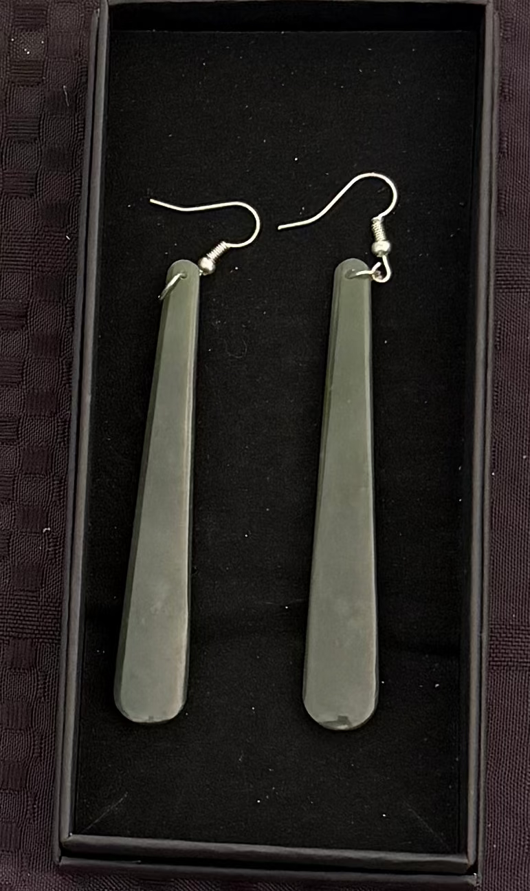 Pair of long, Greenstone earrings in a black box on a textured dark background
