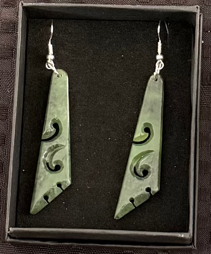 Greenstone earrings with intricate designs in a black box on a textured brown background