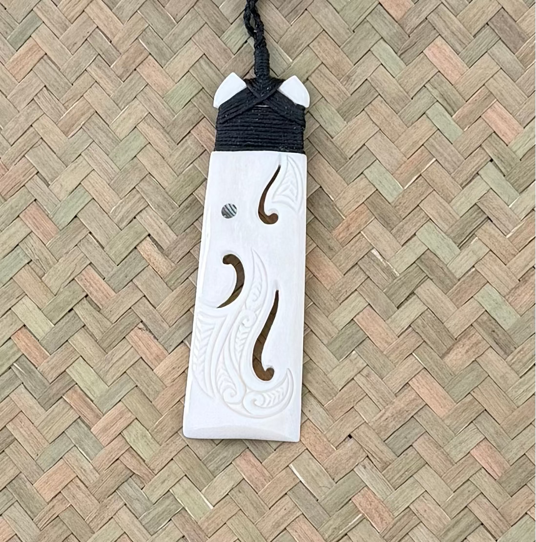 White bone carving pendant with black cord on a woven mat