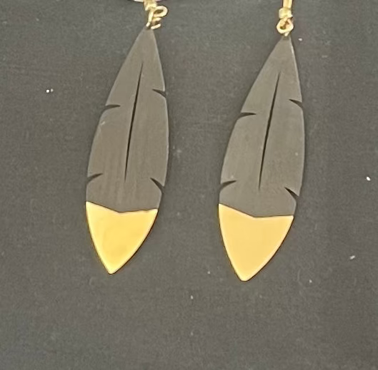 Feather-shaped earrings with gold and black design on a dark background