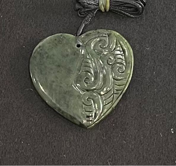 Heart-shaped jade pendant with intricate carvings on a dark background