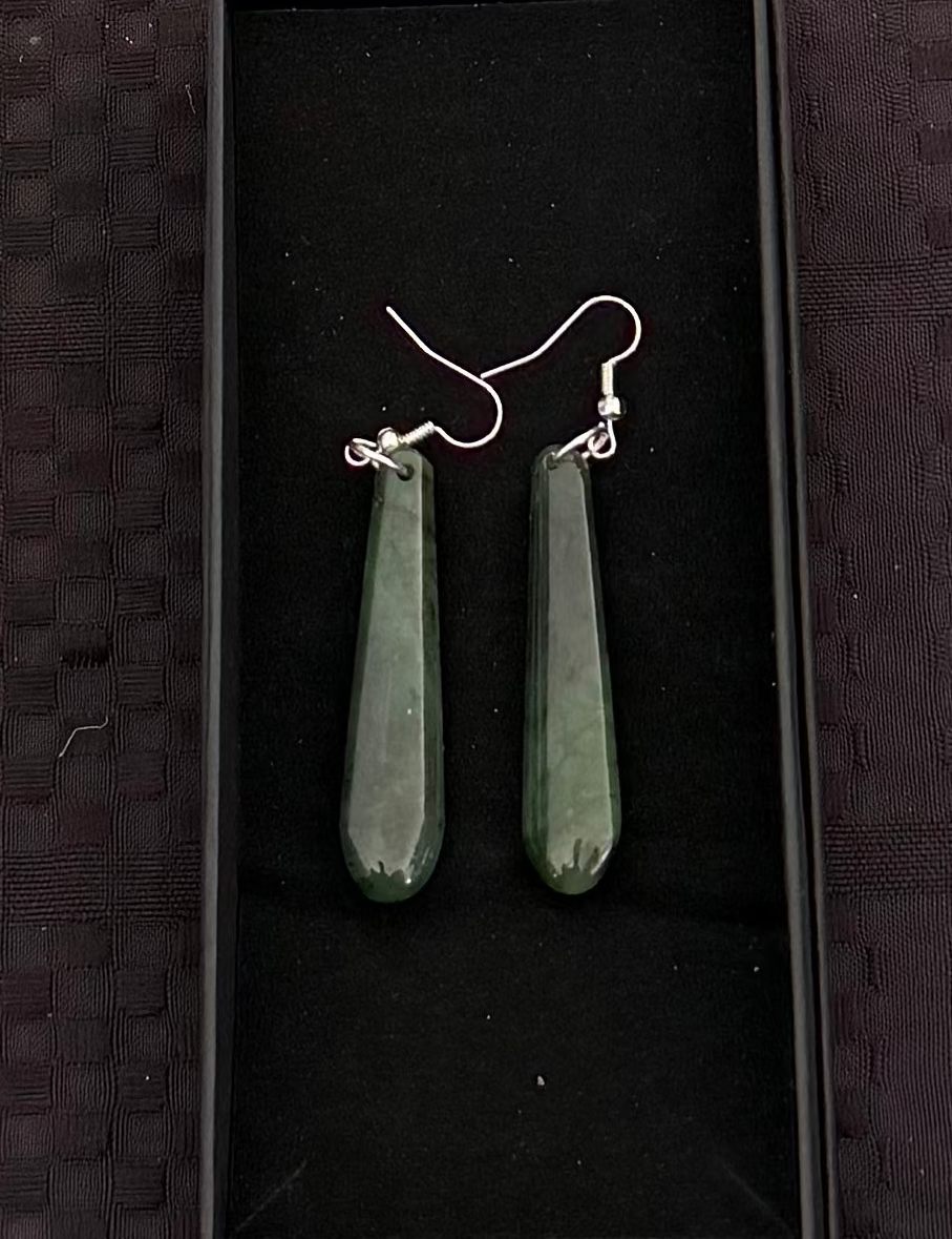 Green jade earrings in a black display box on a textured black background
