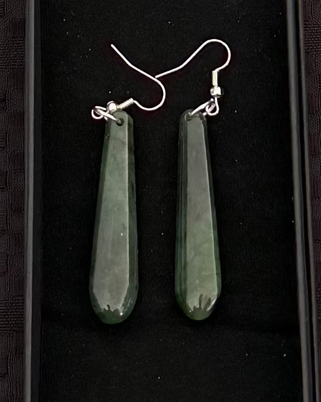 Green jade earrings in a black display box on a textured black background
