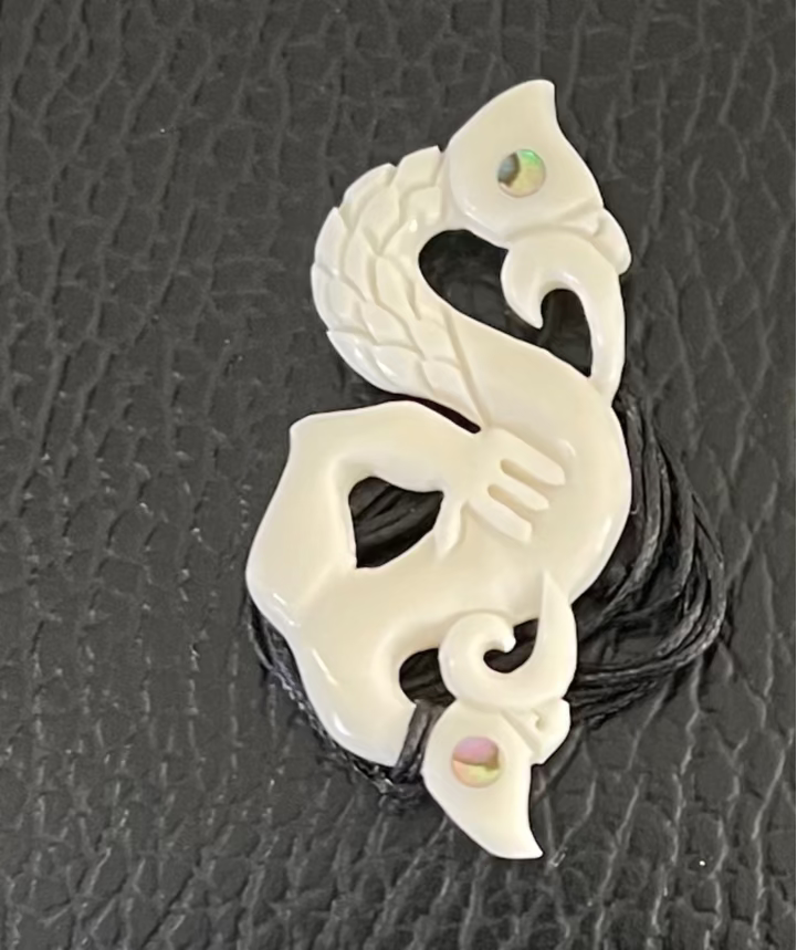 White shaped Manaia pendant on a black textured background