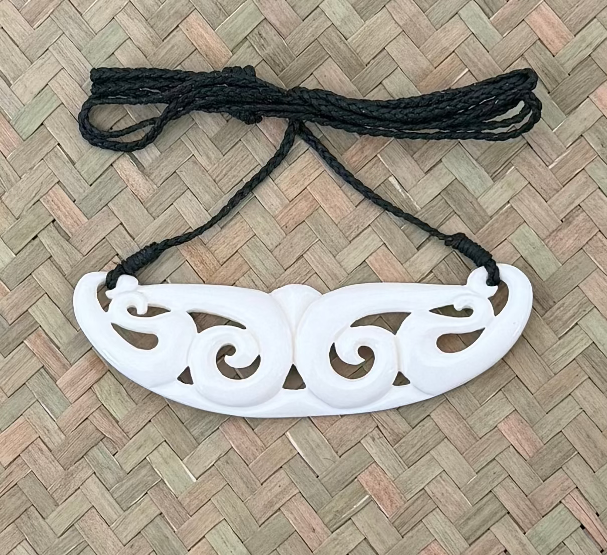 White decorative bone carving with black cord on a woven mat background