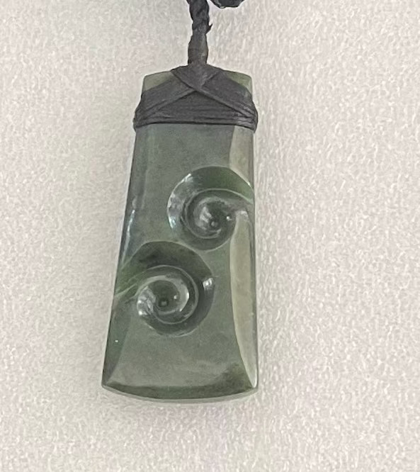 Greenstone jade pendant with spiral design on a white background