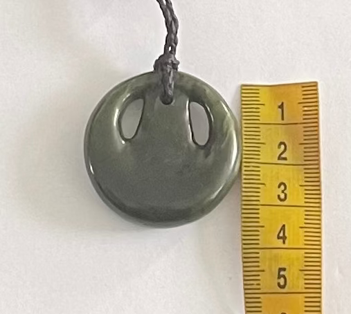 Necklace with a greenstone pendant next to a ruler on a white background