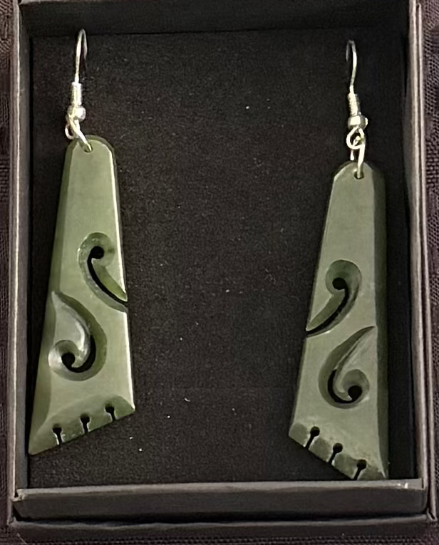 Greenstone earrings with intricate designs in a black box on a textured brown background