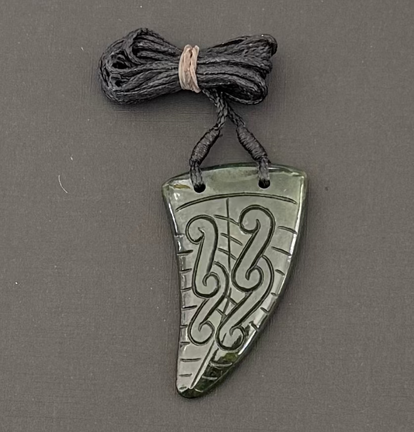 Greenstone shark tooth jade pendant with intricate carvings on a gray background