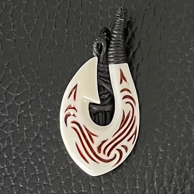 Fish Hook shaped Bone pendant with red patterns on a black textured background