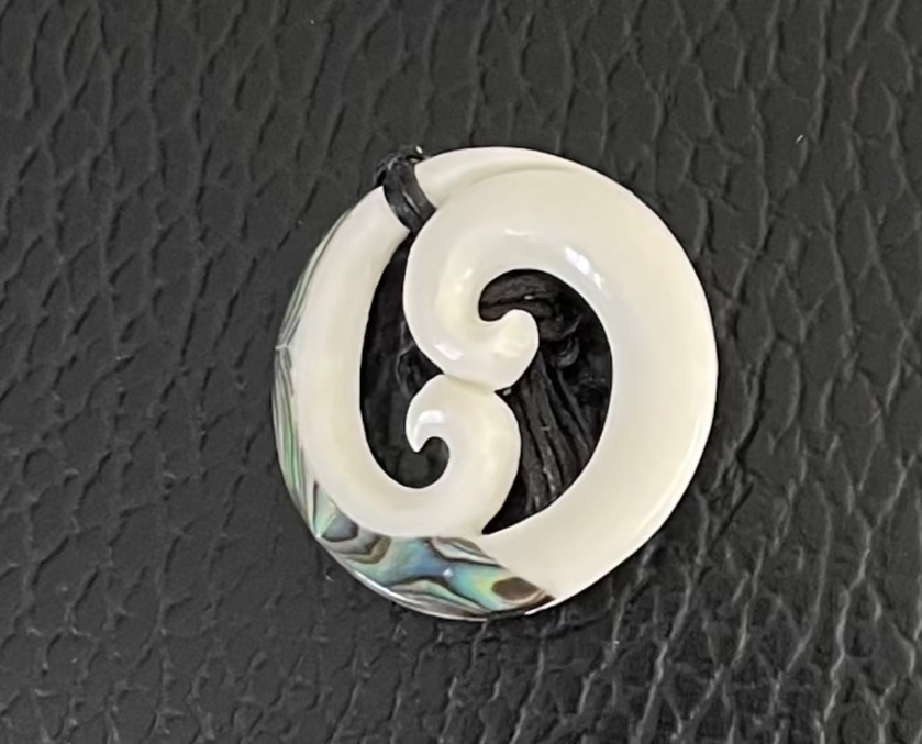 White spiral Koru bone pendant with abalone shell inlay on a black textured background