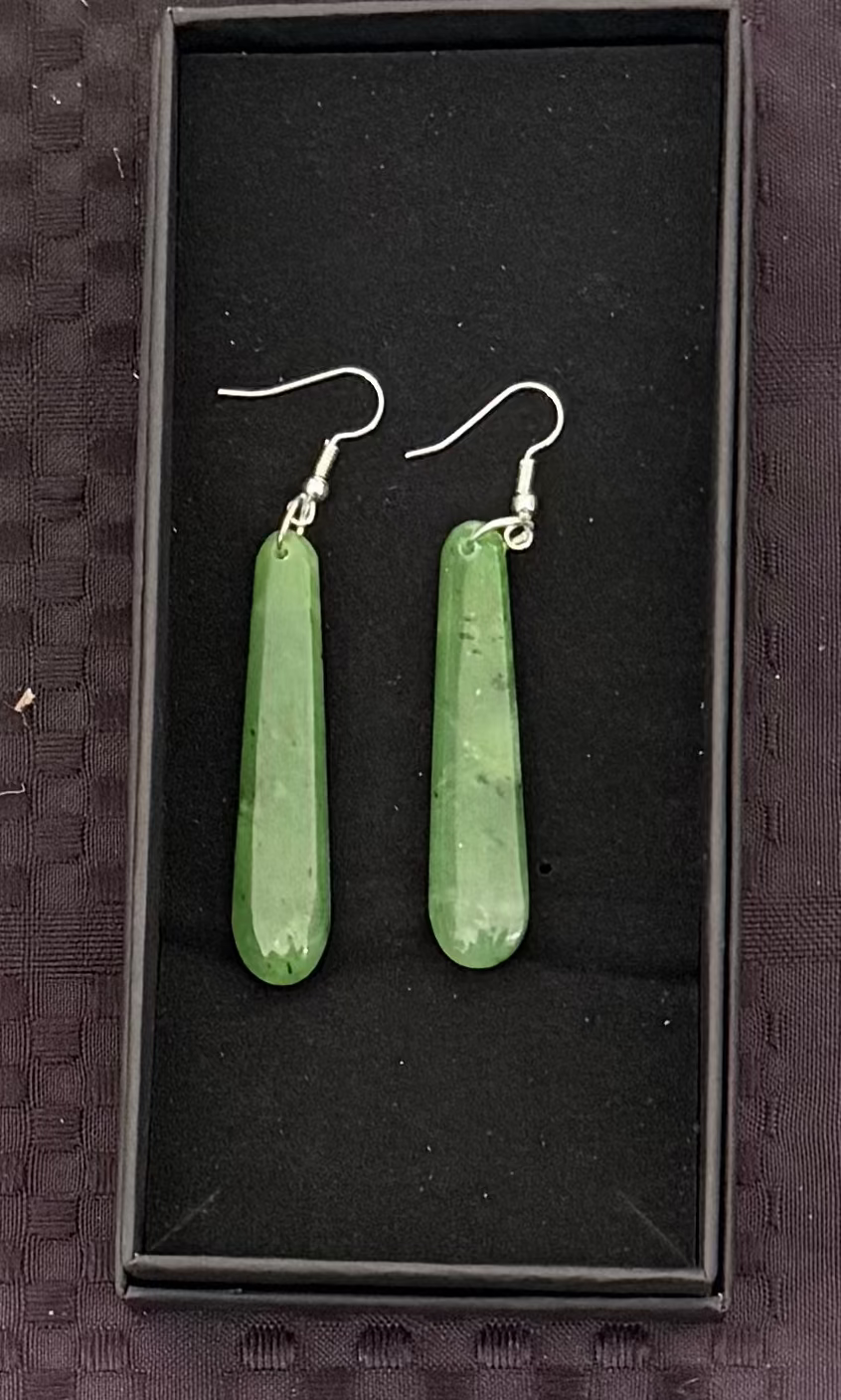 Greenstone earrings in a black display box on a textured brown background