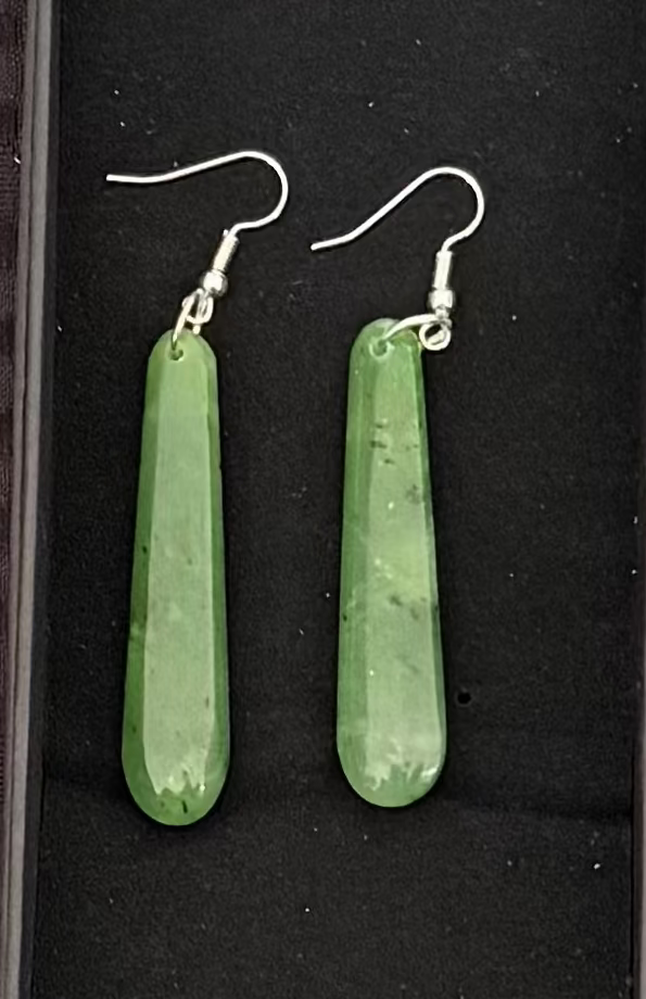 Greenstone earrings in a black display box on a textured brown background