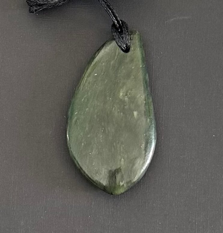 Teardrop-shaped greenstone pendant on a dark gray background