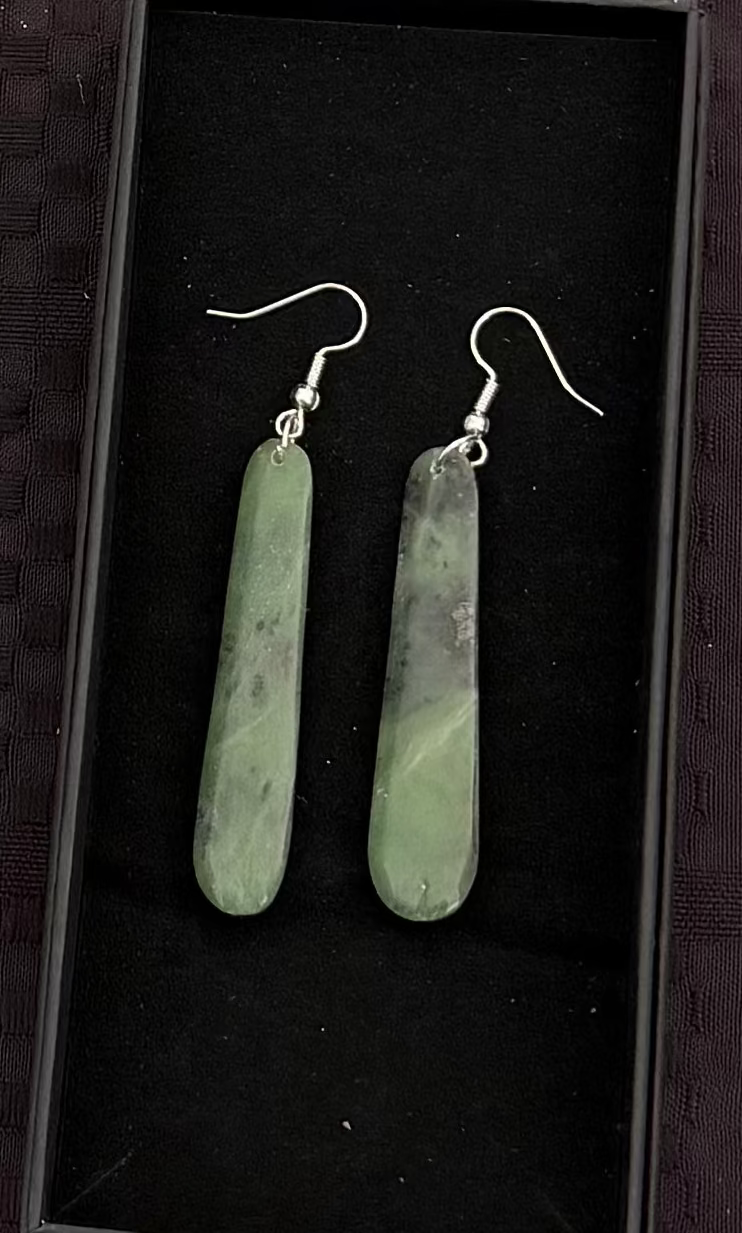 Greenstone bar-shaped earrings in a black display box on a textured black background