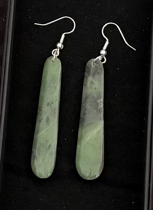 Greenstone bar-shaped earrings in a black display box on a textured black background