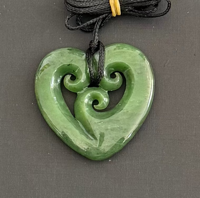 Green jade heart-shaped pendant with spiral design on a gray background