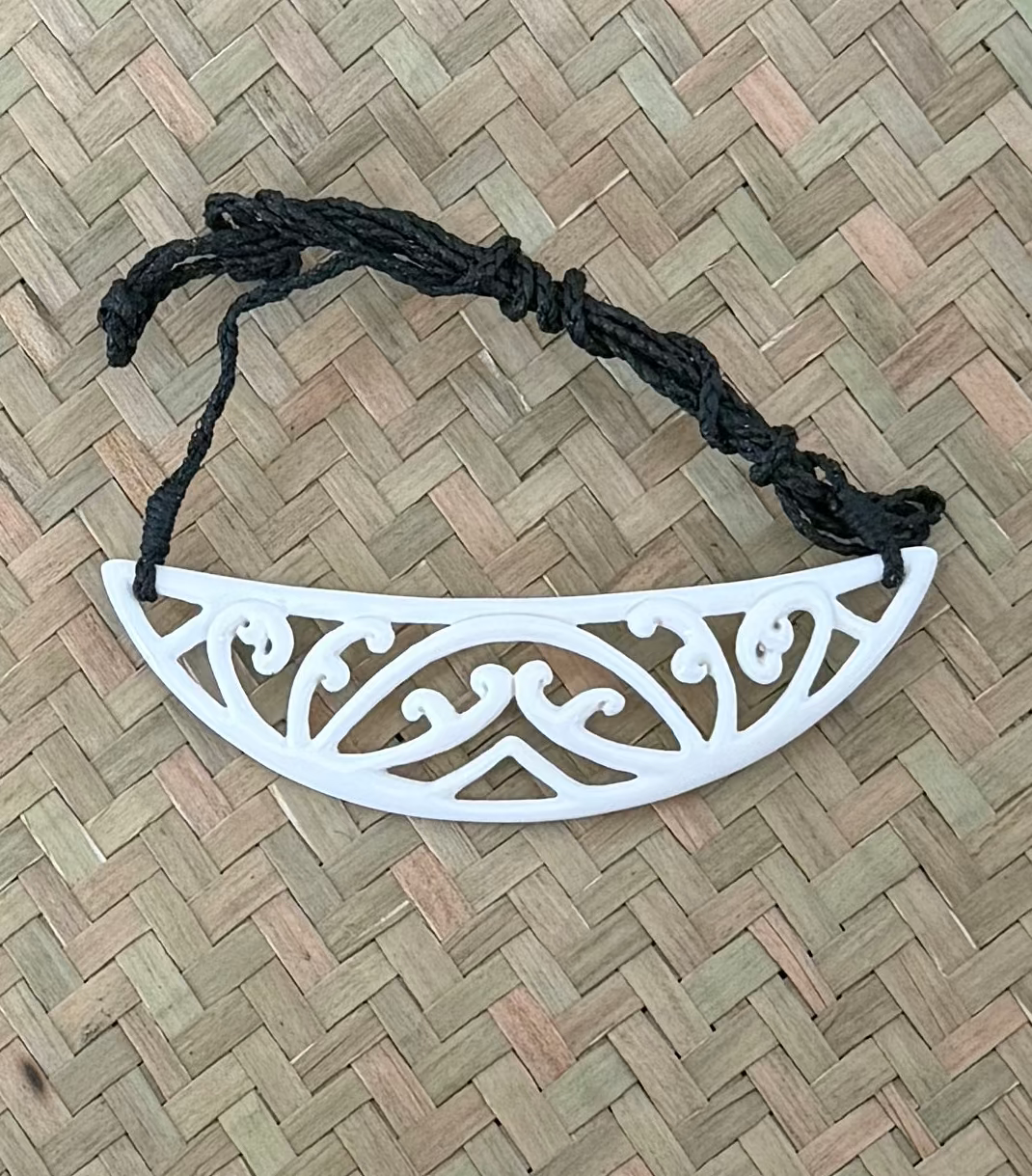 White bone pendant on a black cord against a woven mat background