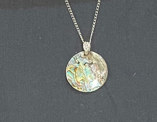 Necklace with a round, iridescent Paua pendant on a dark background
