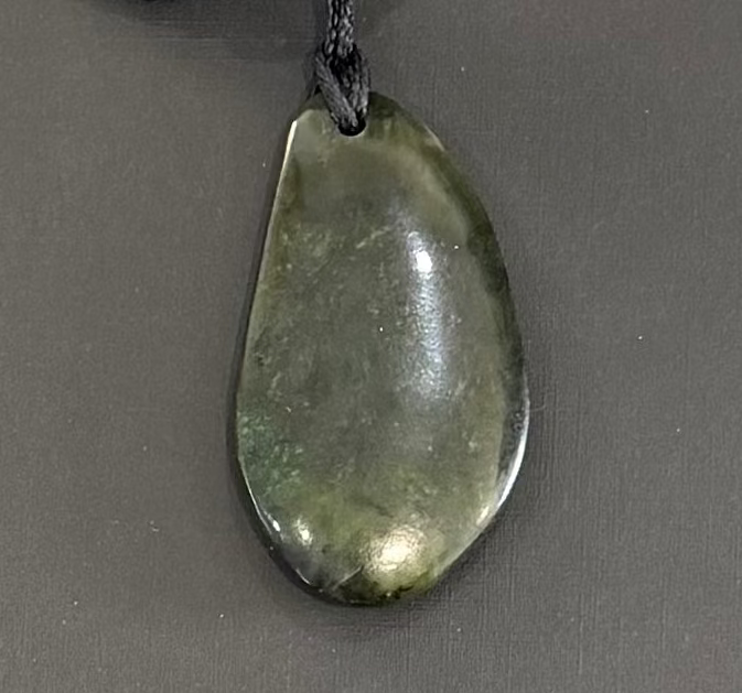 Teardrop-shaped greenstone pendant on a dark gray background