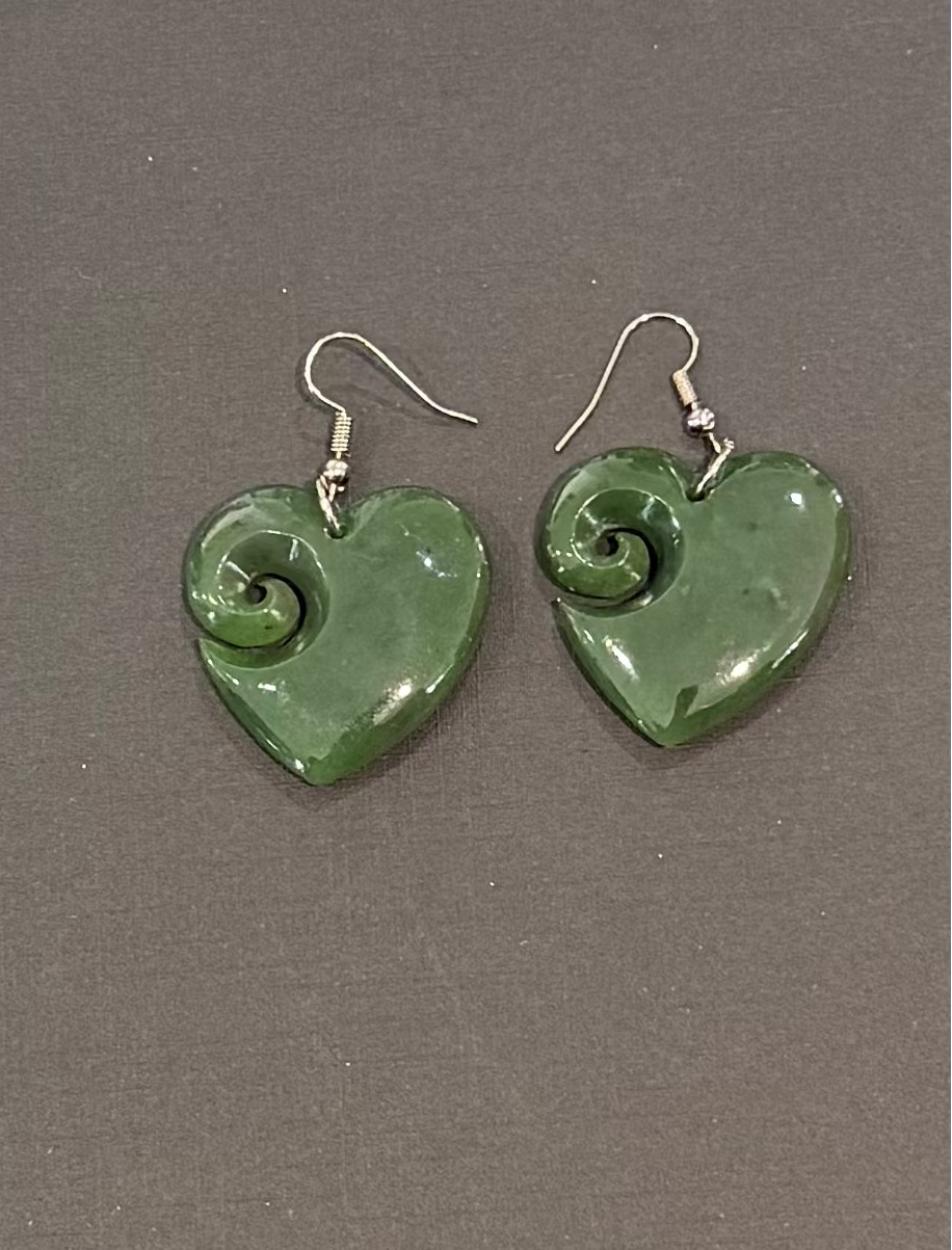 Greenstone heart-shaped earrings with spiral design on a gray background