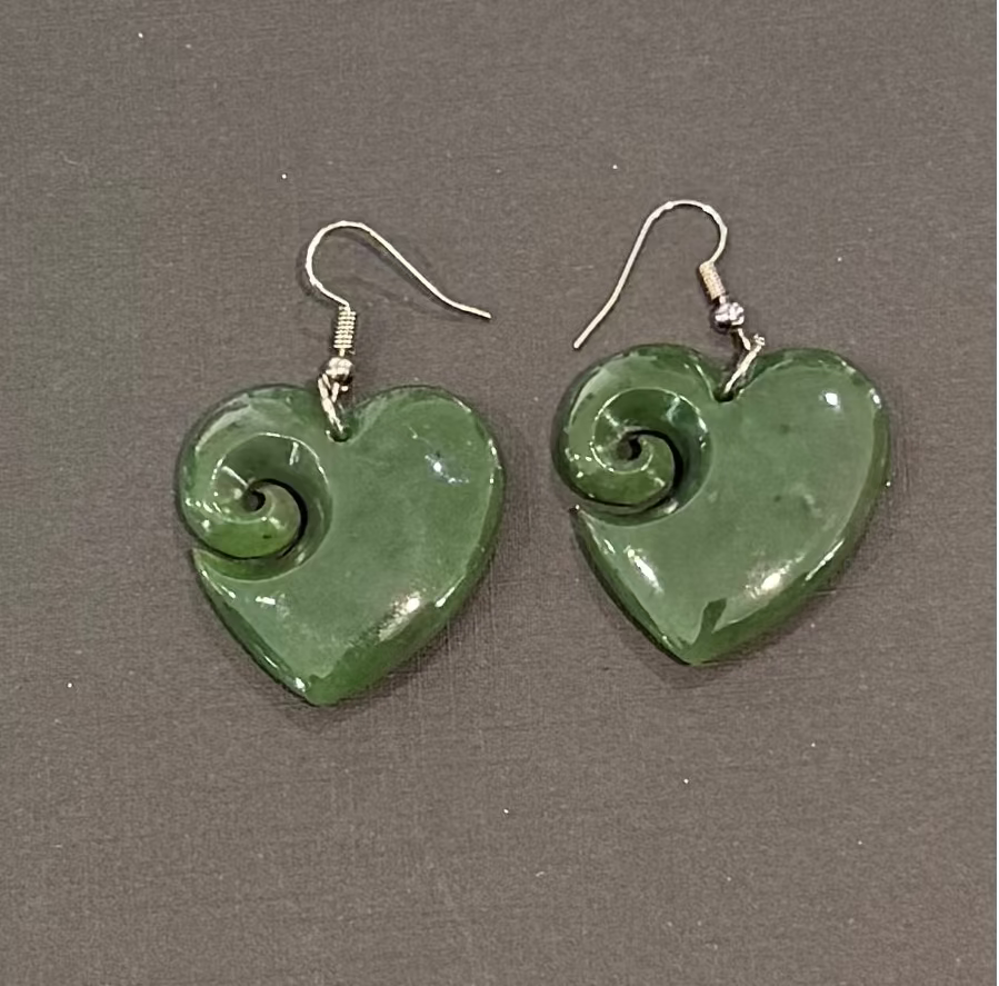 Greenstone heart-shaped earrings with spiral design on a gray background